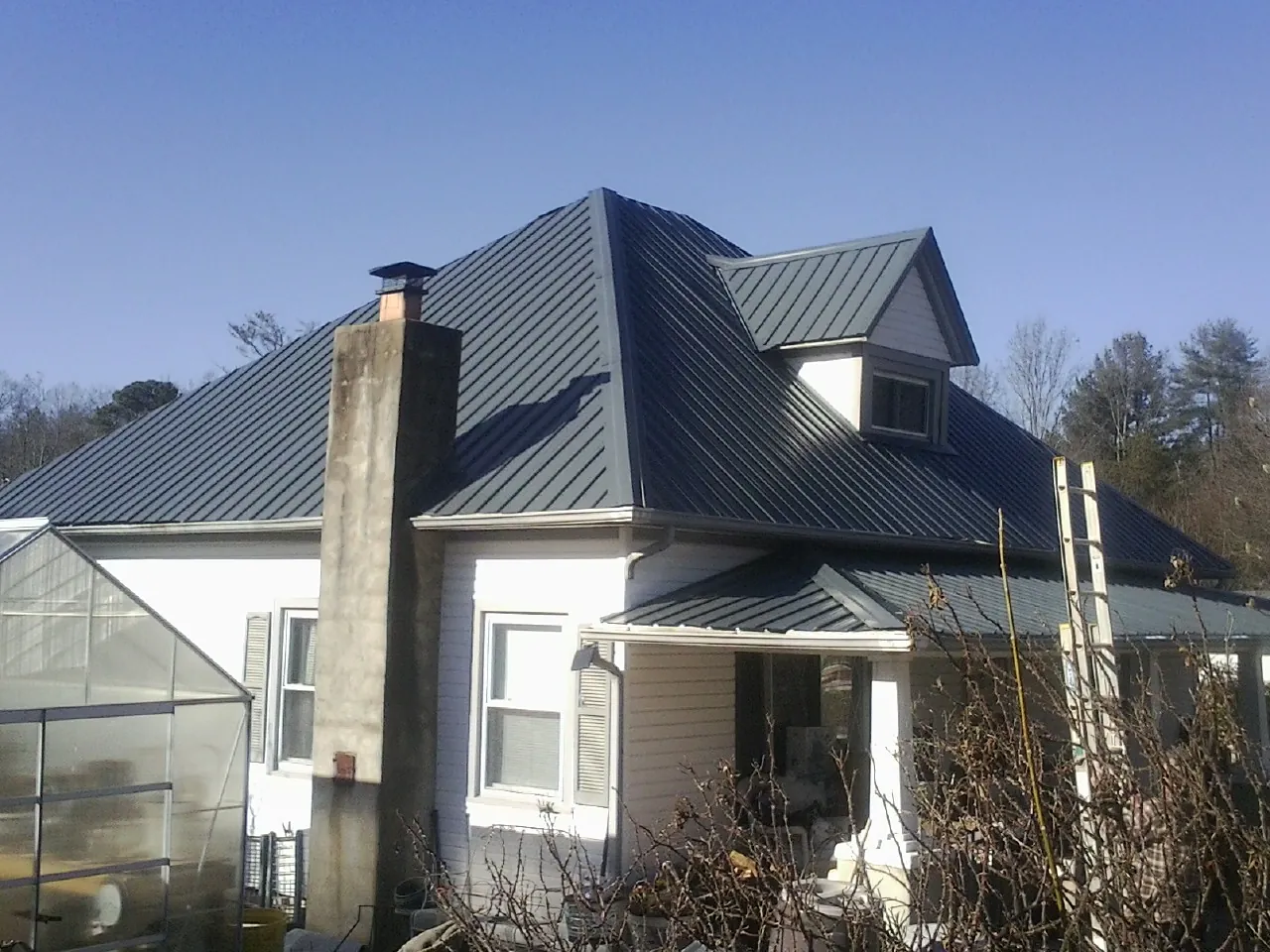 Dark blue standing seam metal roof on a white farmhouse with dormer — Slate & Tile Roof Repair by Roofing Brothers in Harborcreek