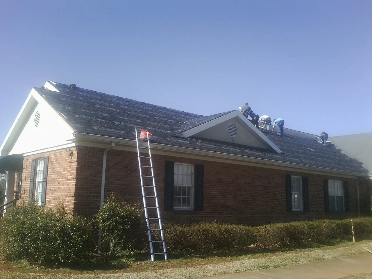 Crew tearing shingles off a brick ranch roof with a ladder set — Metal Roof Repair work by our crew in Harborcreek