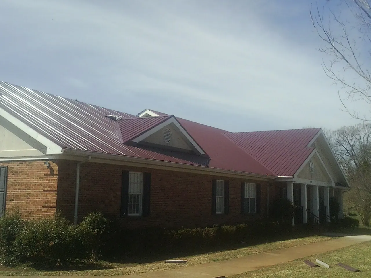 Red metal roof with gabled entries on a long brick building, from a Hail Damage Roof Repair job in Harborcreek