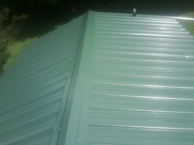 New green metal panels meeting at the ridge of a roof — Flat Roof Repair work by our crew in Harborcreek