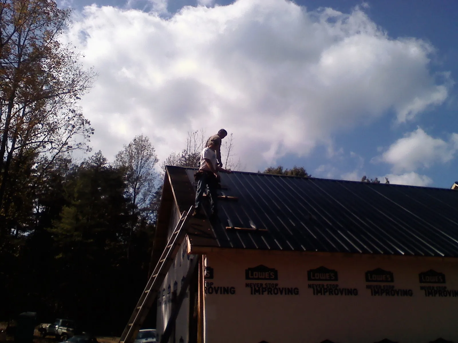 Roofer fastening dark metal panels high against a cloudy sky, from a Roof Inspection job in Harborcreek