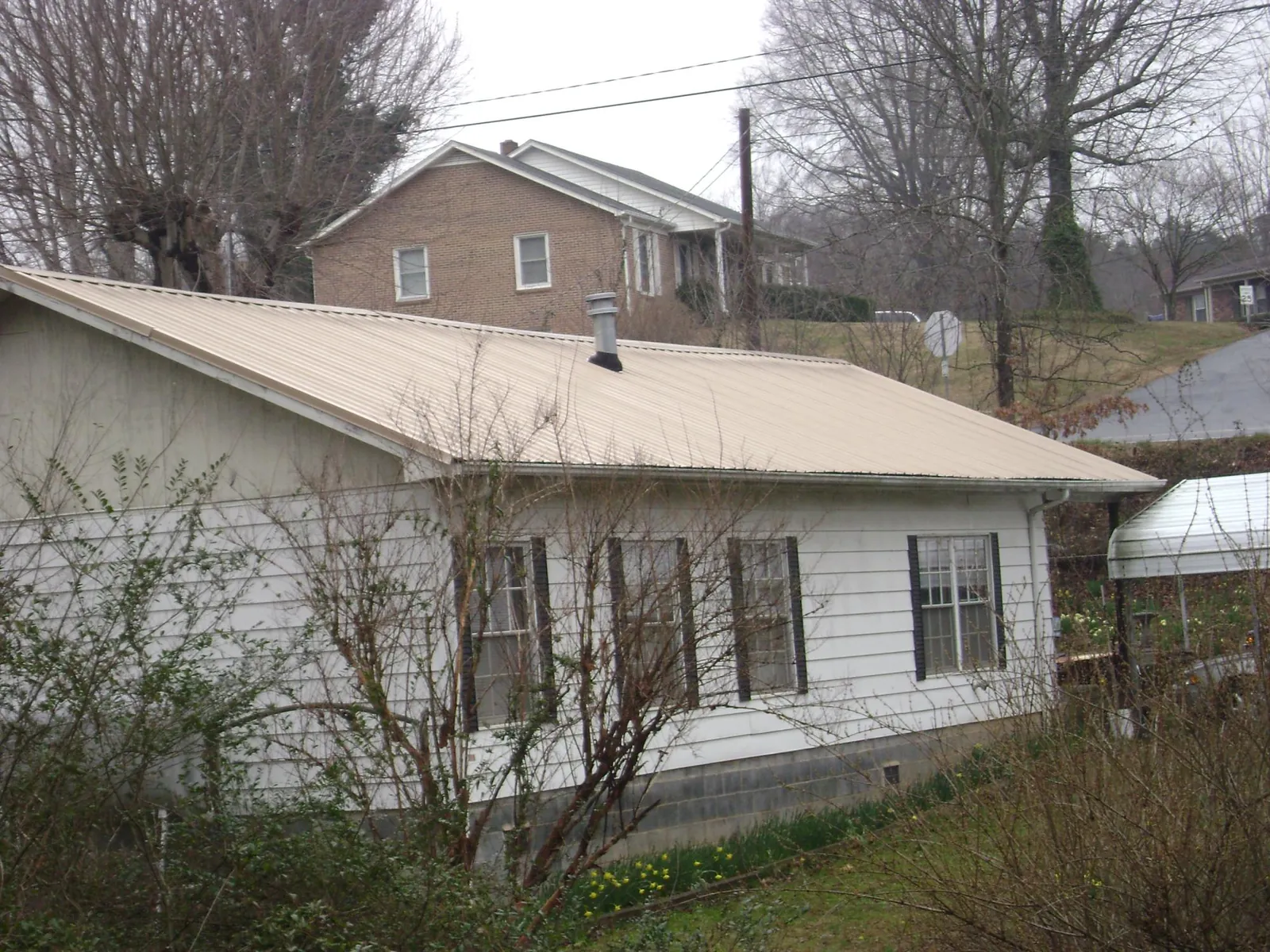 Tan metal roof on a white sided house set into a hillside — Commercial Roofing by Roofing Brothers in Harborcreek