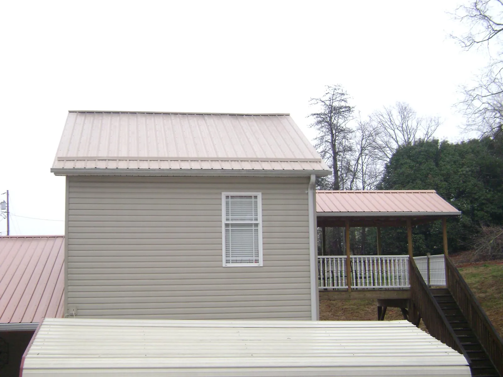 Tan metal roofs on a two story addition and attached porch, from a Roof Replacement job in Harborcreek