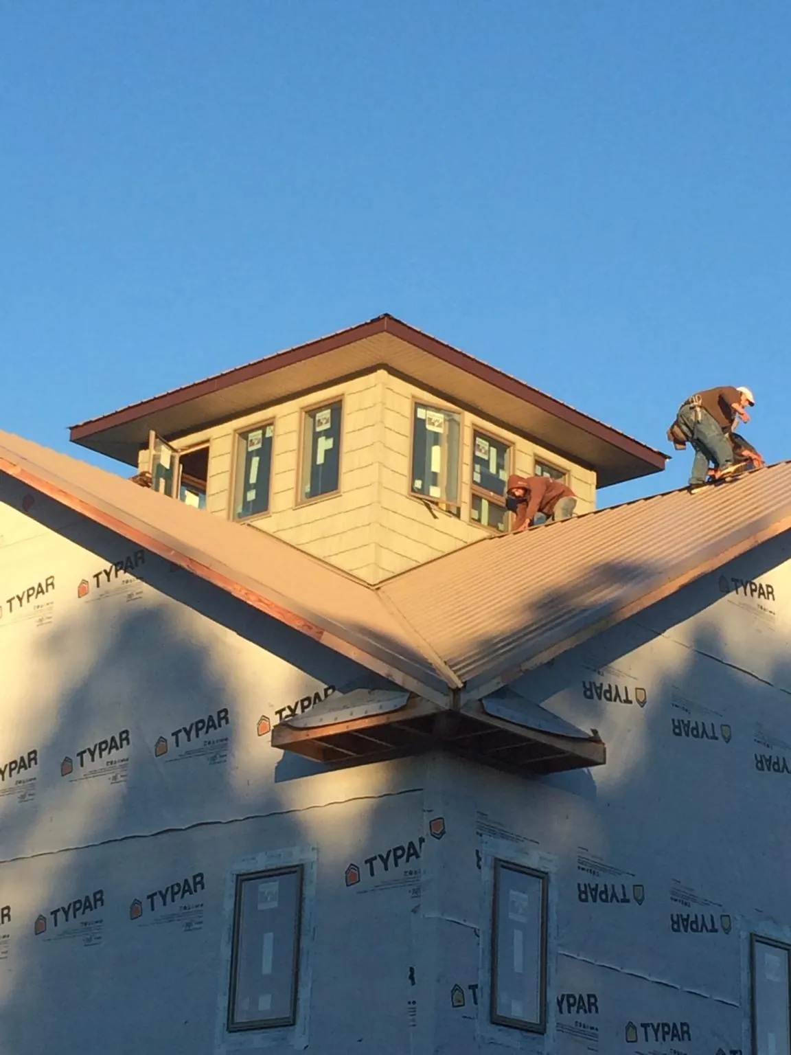 Roofers working around a rooftop cupola on a new metal roof at sunset — Roof Waterproofing in Harborcreek by Roofing Brothers
